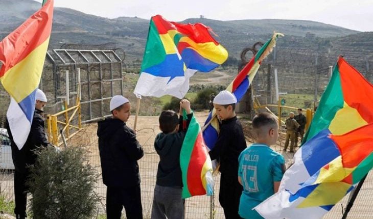 Druze youth wave flags near Israeli soldiers at the border crossing in Majdal Shams as a delegation from Syria arrives, March 14, 2025. (AFP)