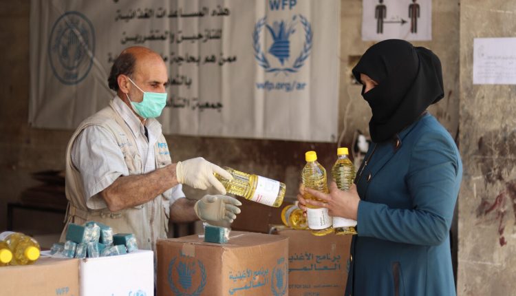 A member of the World Food Program (WFP) is distributing food aid to a woman in Raqqa Governorate, north Syria, in June 2020 – WFP