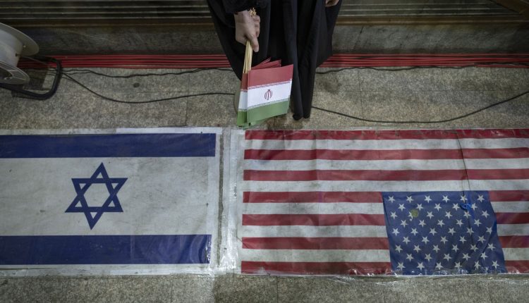 An Iranian woman stands between U.S. and Israeli flags during a ceremony in Tehran tied to a state-backed "Lady of the Year" program honoring women's achievements. – Axios/Getty Images
