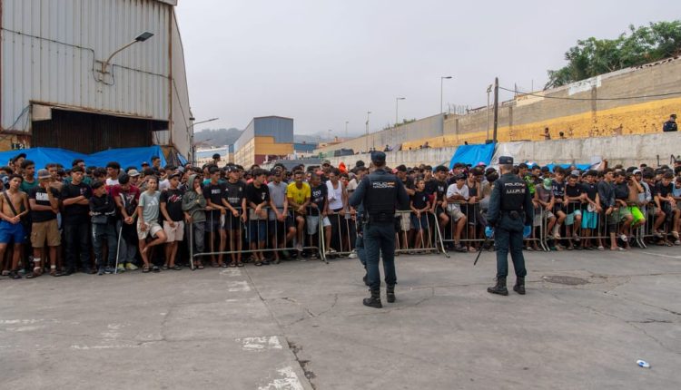 Spanish national police officers stand as migrants wait during a distribution of food by volunteers at an industrial site in Ceuta on Sept. 2, 2026. – AFP via Getty Images