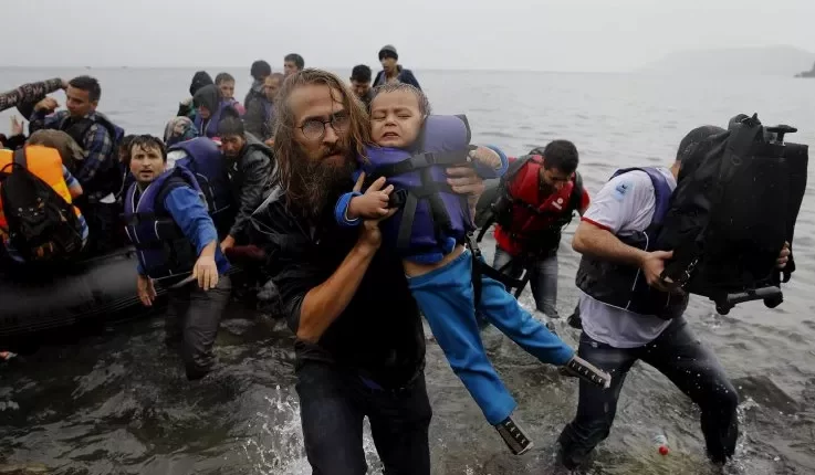 متطوع يحمل طفلاً سورياً لاجئاً من زورق مكتظ بعد أن عبر المهاجرون جزءاً من بحر إيجه من تركيا إلى جزيرة ليسبوس اليونانية- رويترز