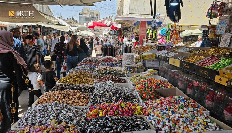 القامشلي – سكان يمرون بجانب ضيافة العيد وسط سوق شعبي - نورث برس