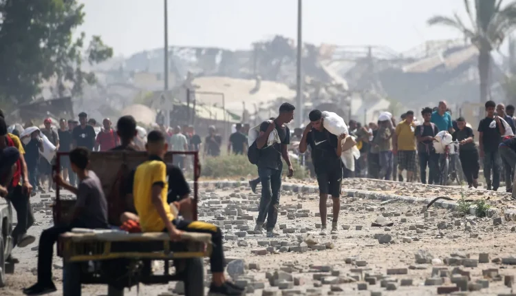 فلسطينيون نازحون في مخيم النصيرات للاجئين يحملون طروداً غذائية ومواد أخرى تمكنوا من الحصول عليها من نقطة توزيع مساعدات - أ ف ب