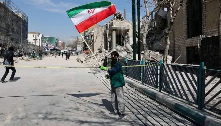 طفل يحمل علماً إيرانياً بجانب موقع تعرض لغارة أميركية في مارس الفائت - رويترز